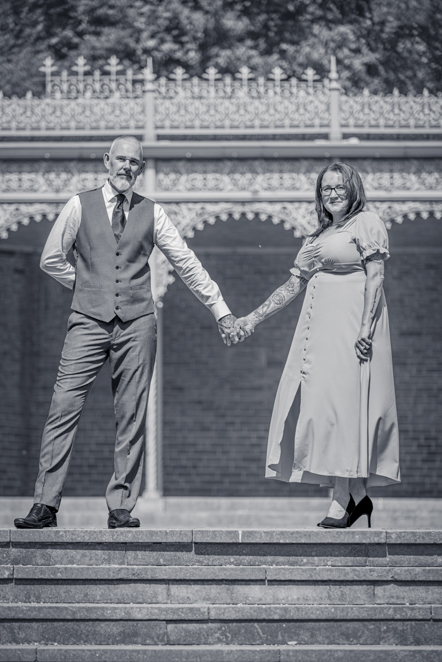 Black-and-white image of Couple standing apart but holding hands together with bandstand behind them