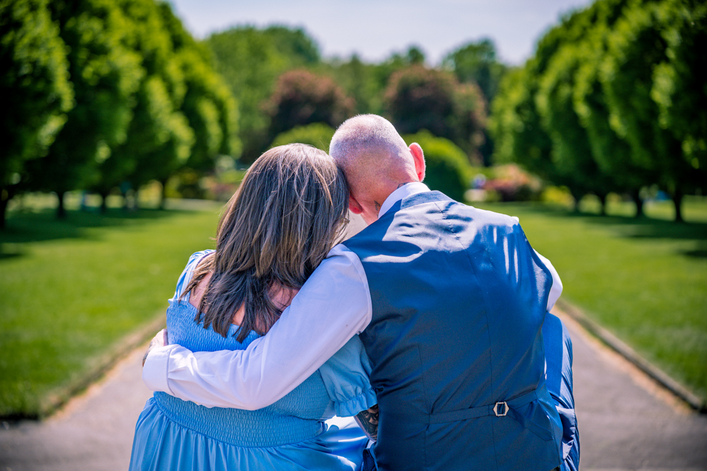 Back view of a couple sitting on steps with man's arm round the woman’ back. With with trees on either side of them taken by Manchester Photographer Wedding Rebekah Morecroft