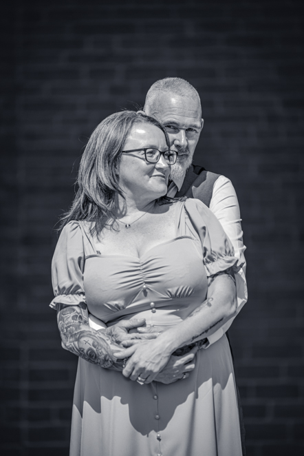 Black-and-white image of Man wrapping his arms round the front of his fiance