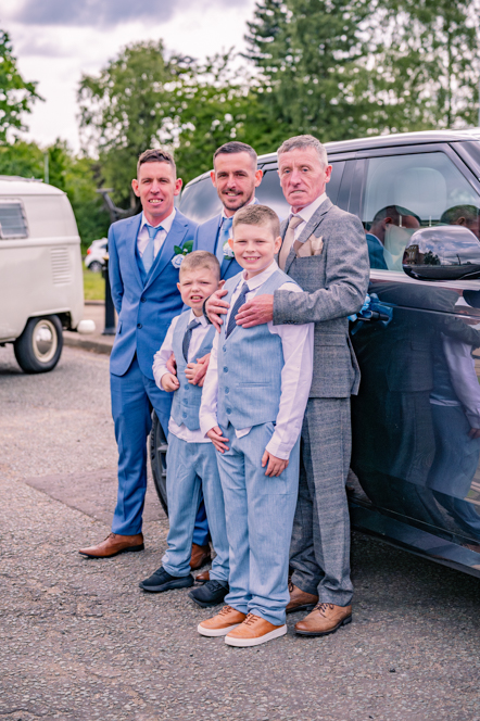 The groom, his father. Best man and two page boys standing next to a grey Range Rover