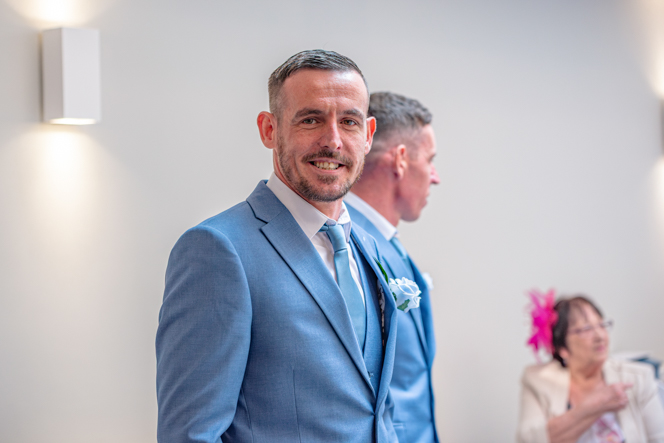 The groom smiling with guests behind him