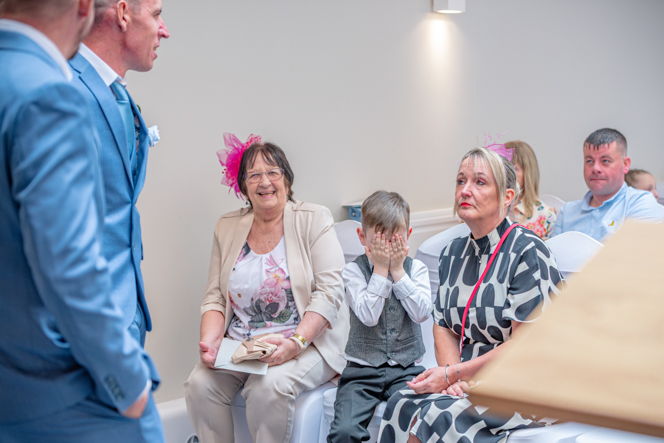 Group of wedding guests sitting in their chairs with one little boy holding his hands over his face