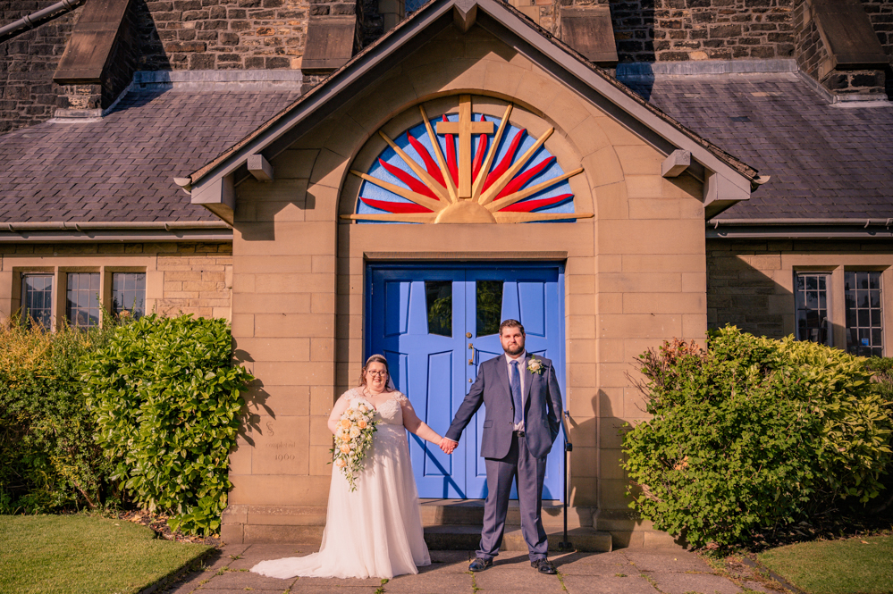 Bride and groom holding hands at a distance with church doors behind them taken by Manchester Photographer Wedding Rebekah Morecroft