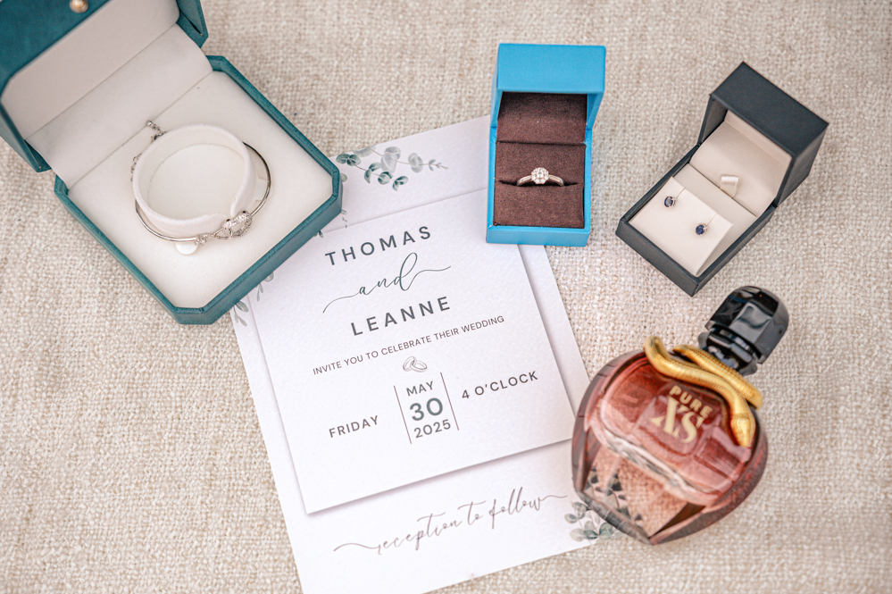 The bride’s jewellery including her engagement ring, earrings and bracelet. Her perfume and a wedding invite