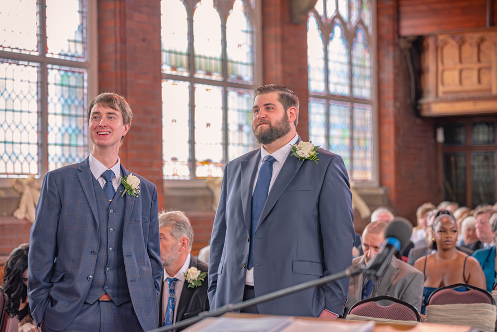 Groom and best man waiting at the front of the church with guests sitting behind them