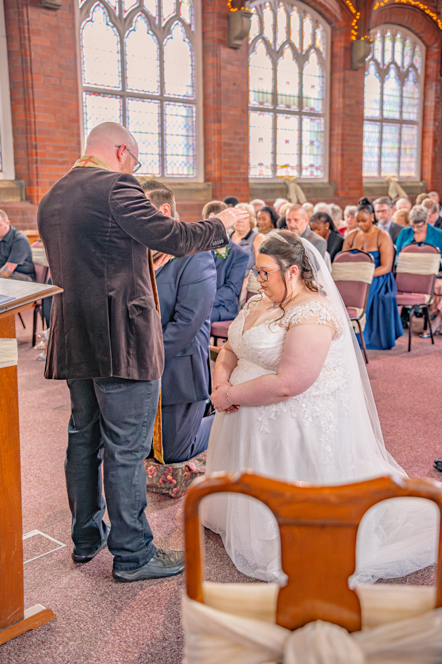 Bride and groom kneeling while reverend prays for them