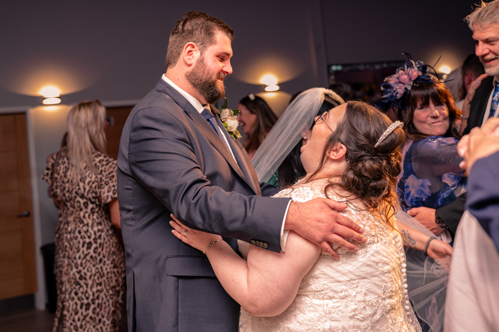 Bride and groom's first dance with wedding guests dancing on the dance floor. Bride also laughing
