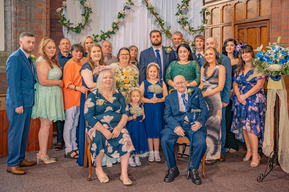 Bride and groom with both families at church wedding in Bury