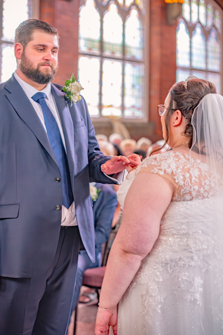 Bride placing ring on groom’s hand during church ceremony in Bury