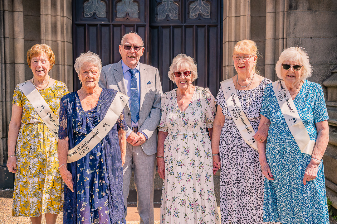 Four original bridesmaids and couple portrait outside St Peter’s Church, Ashton-under-Lyne, during traditional Christian wedding vow renewal celebration