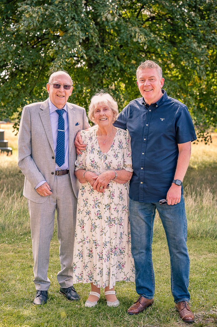 Older couple and son portrait at St Peter’s Church grounds, Ashton-under-Lyne, traditional Christian wedding vow renewal