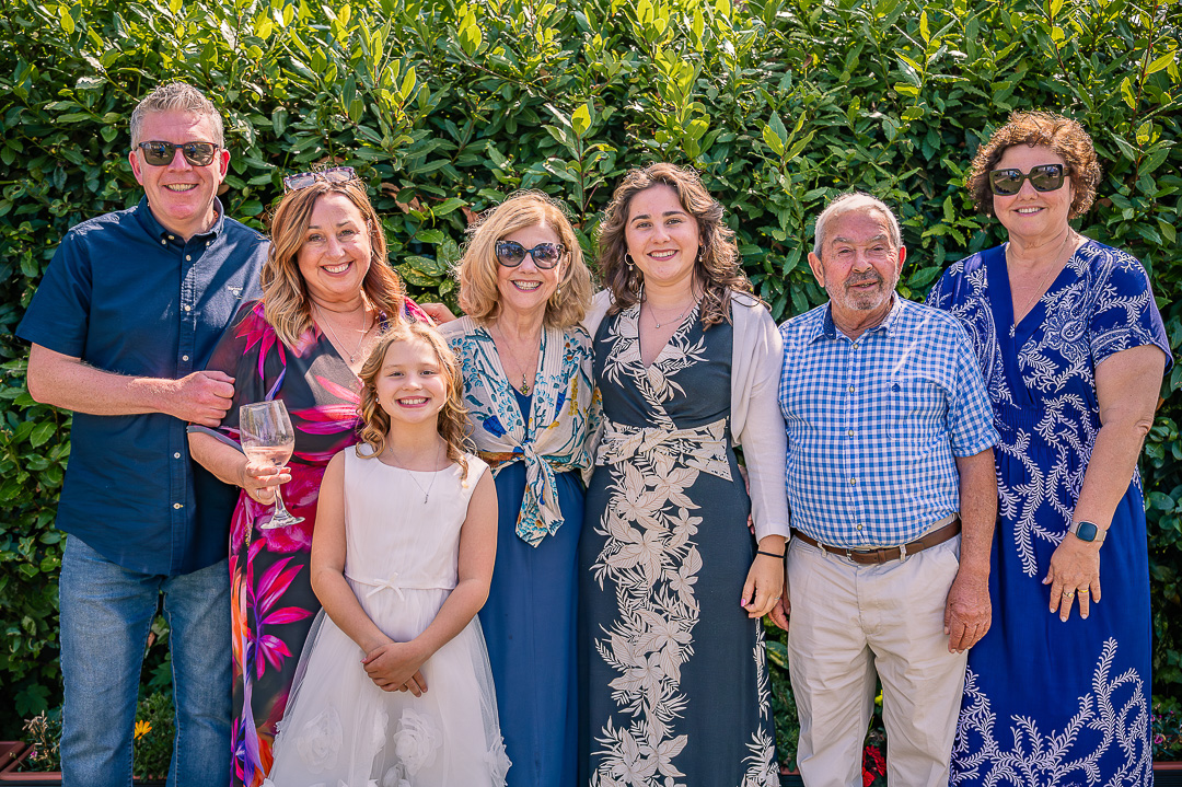 Woman standing with her daughters, their husbands and two granddaughters for a family portrait.