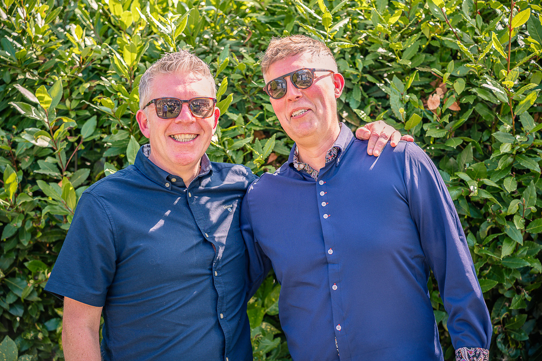 Two men wearing sunglasses posing together outside at the reception.