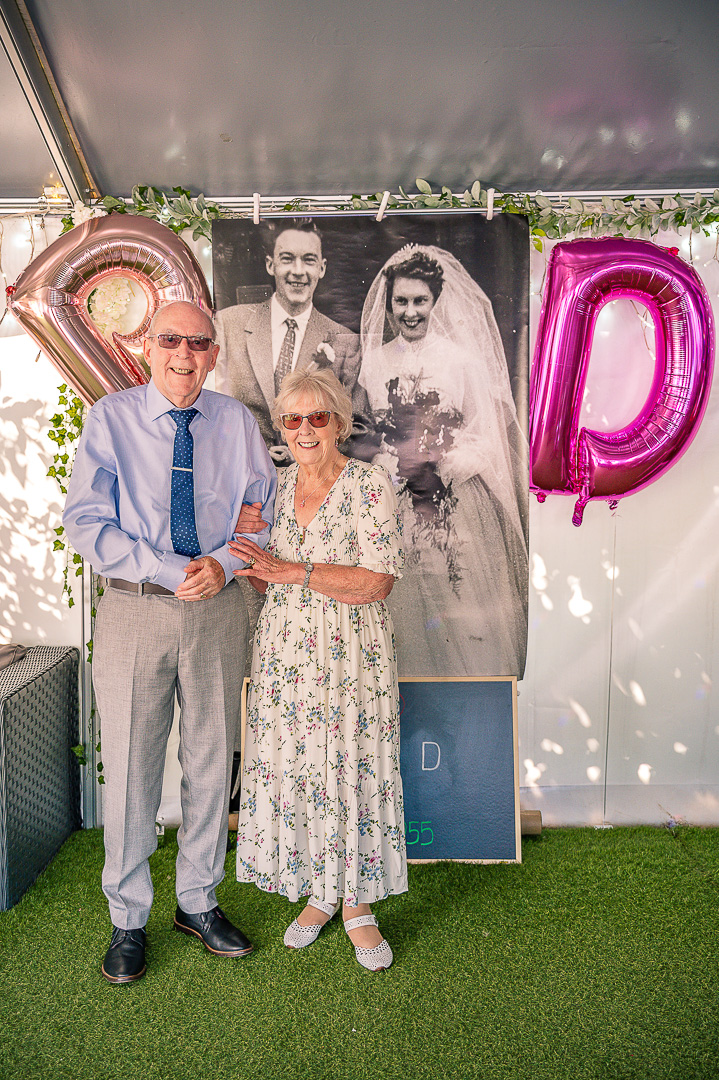Older couple standing in front of an enlarged photograph from their original wedding day.