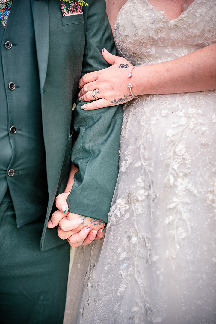 Close-up of the bride and groom holding hands with her arm linked through his