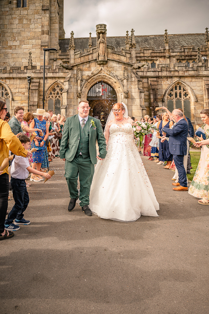 Newly married couple smiling as guests throw confetti outside the church in Rochdale