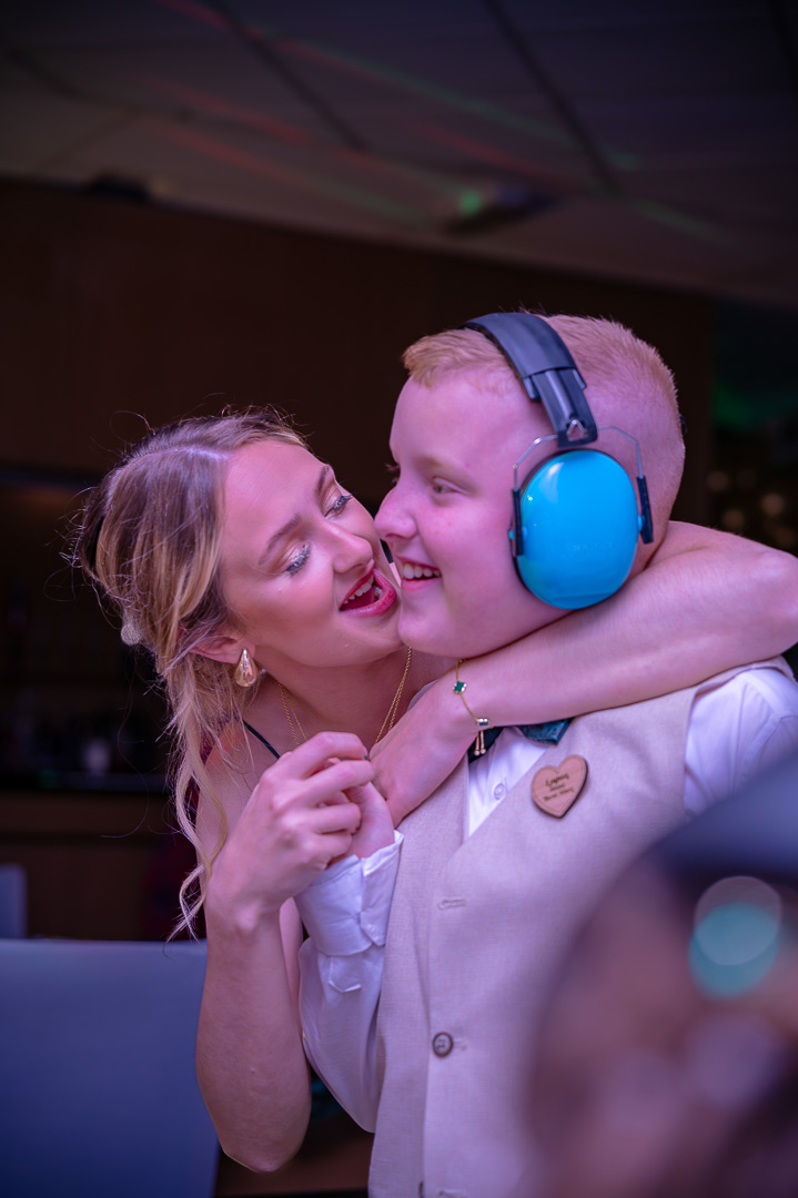 Woman hugging her young brother, who is wearing ear defenders, on the dance floor at a family-focused, traditional wedding