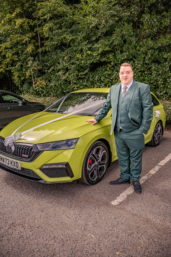 Groom resting his hand on a lime green wedding car outside the Royal Toby Hotel