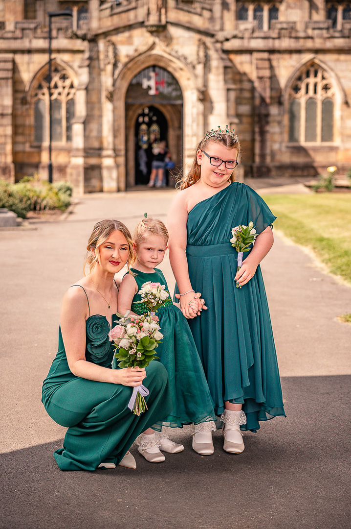 Bridesmaid crouching with two young bridesmaids in green dresses outside St Chad’s Church before the ceremony