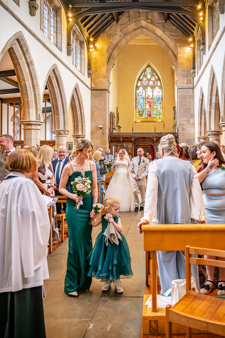 Bridesmaid and flower girl walking down the aisle at St Chad’s Church during a classic Christian wedding