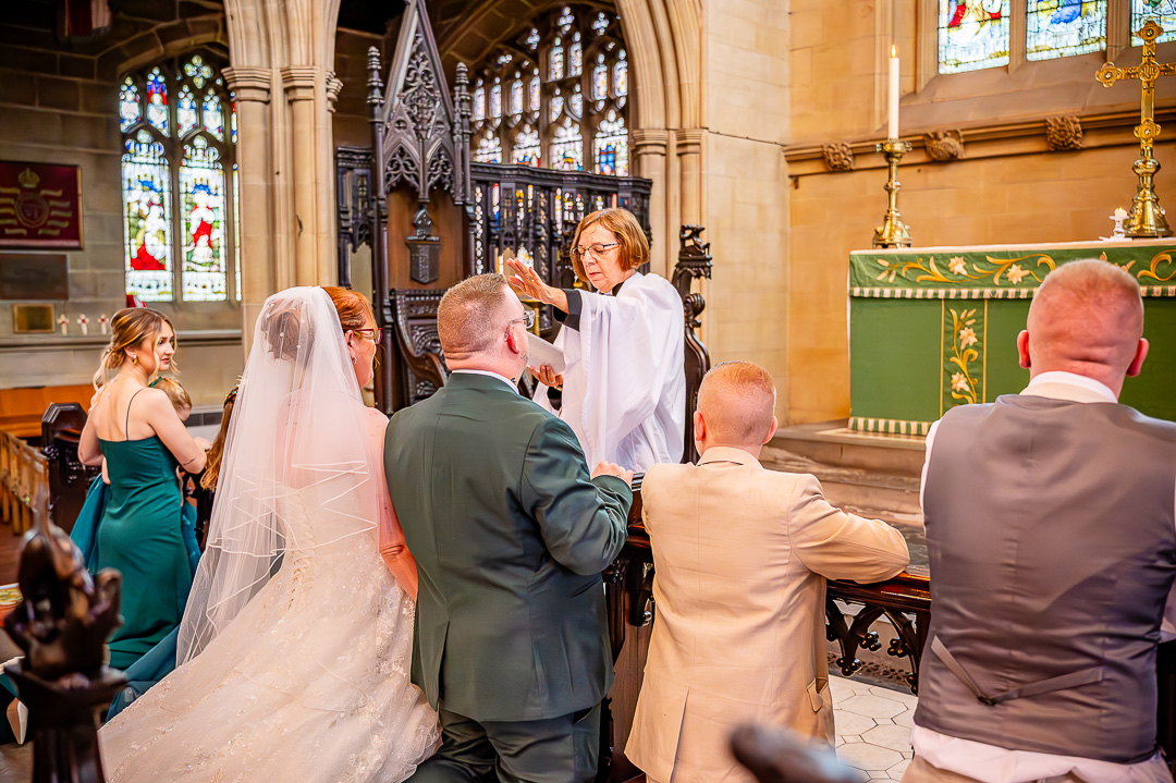 Vicar blessing the bride and groom as they kneel at the altar during the Christian ceremony