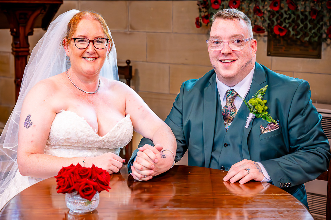 Bride and groom seated together holding hands and smiling during the signing of the register