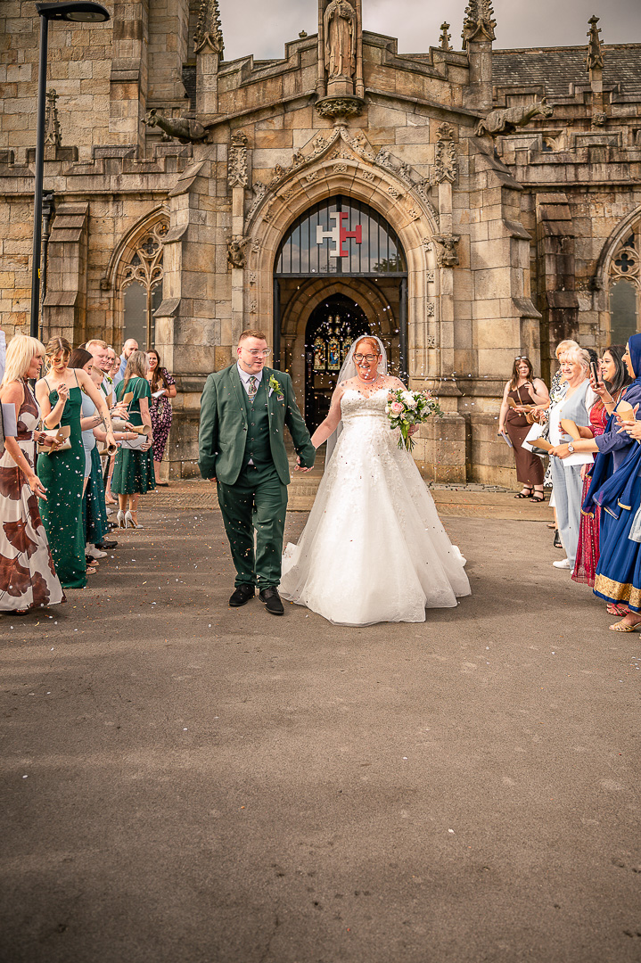 Bride and groom walking through confetti outside St Chad’s Church in Greater Manchester