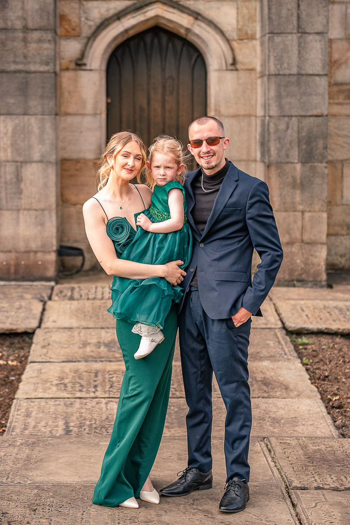 portrait of couple holding their daughter, outside St Chad’s Church in Rochdale
