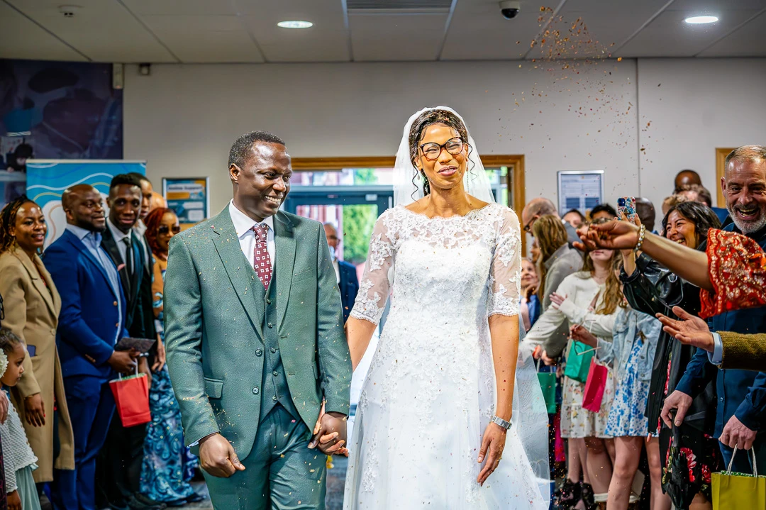 Couple smiling during Confetti celebrations inside the foyer at William Hulme's Grammar School during Bea and Abraham's wedding blessing in Manchester