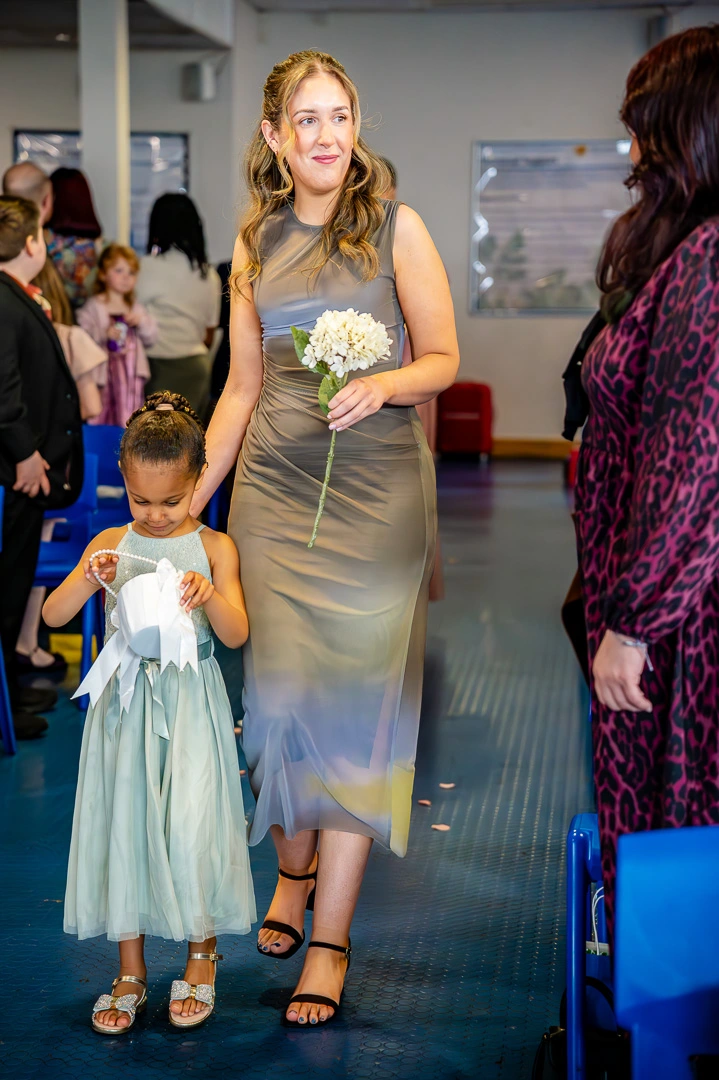 Flower girl walking down the aisle at Bea and Abraham's wedding blessing at William Hulme's Grammar School, Manchester